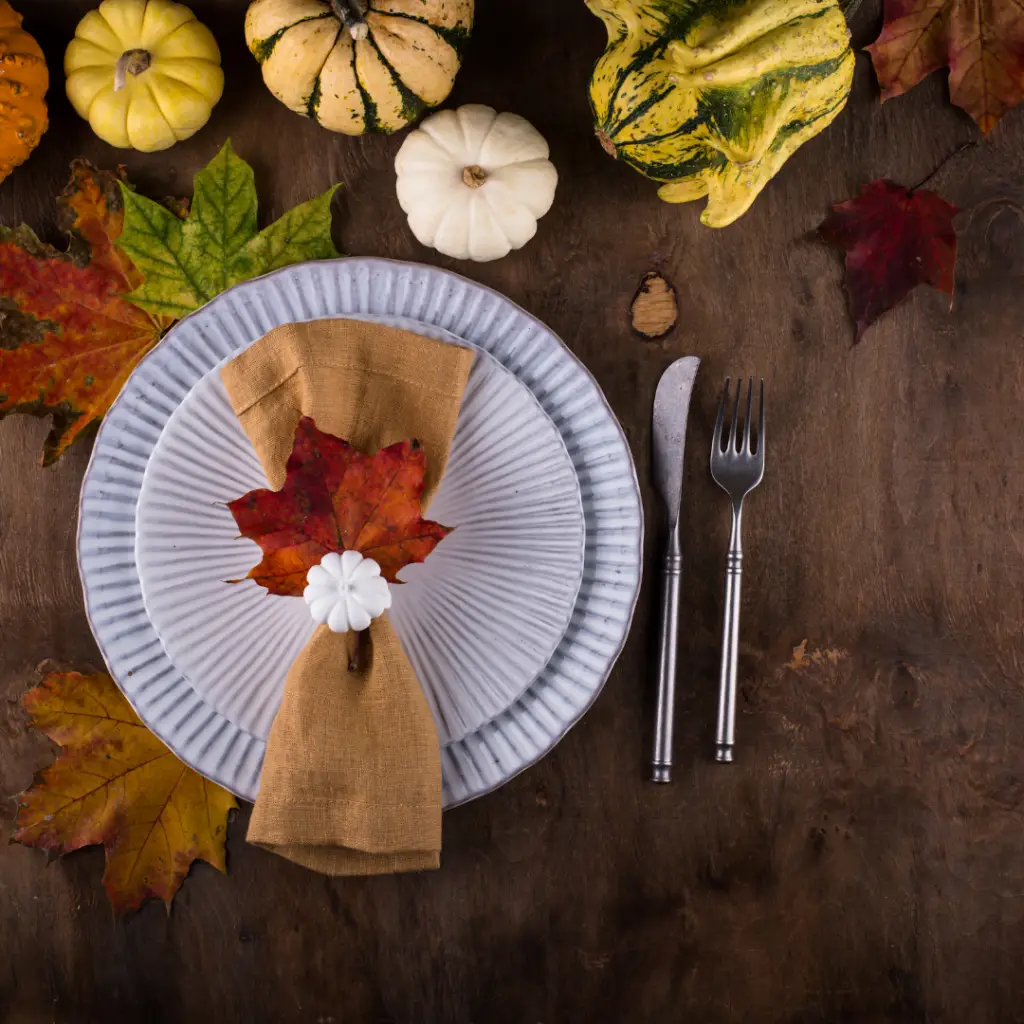 White plates with autumn leaves and small pumpkins on a table